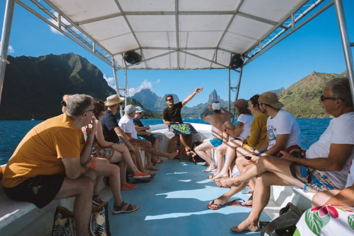 Group of people sitting on a boat in a scenic mountain and ocean setting.