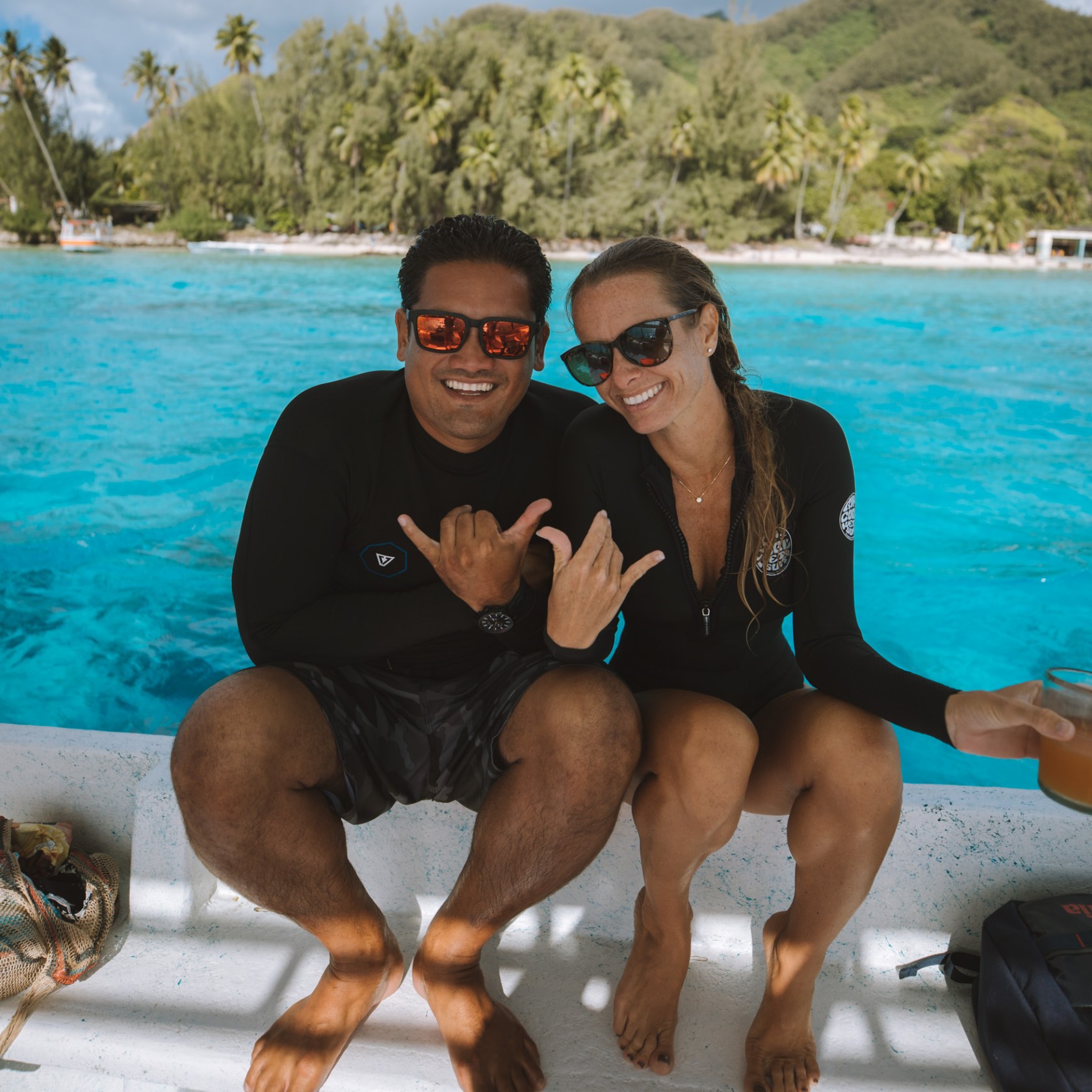 Two people in swimsuits on a boat, smiling with ocean background.
