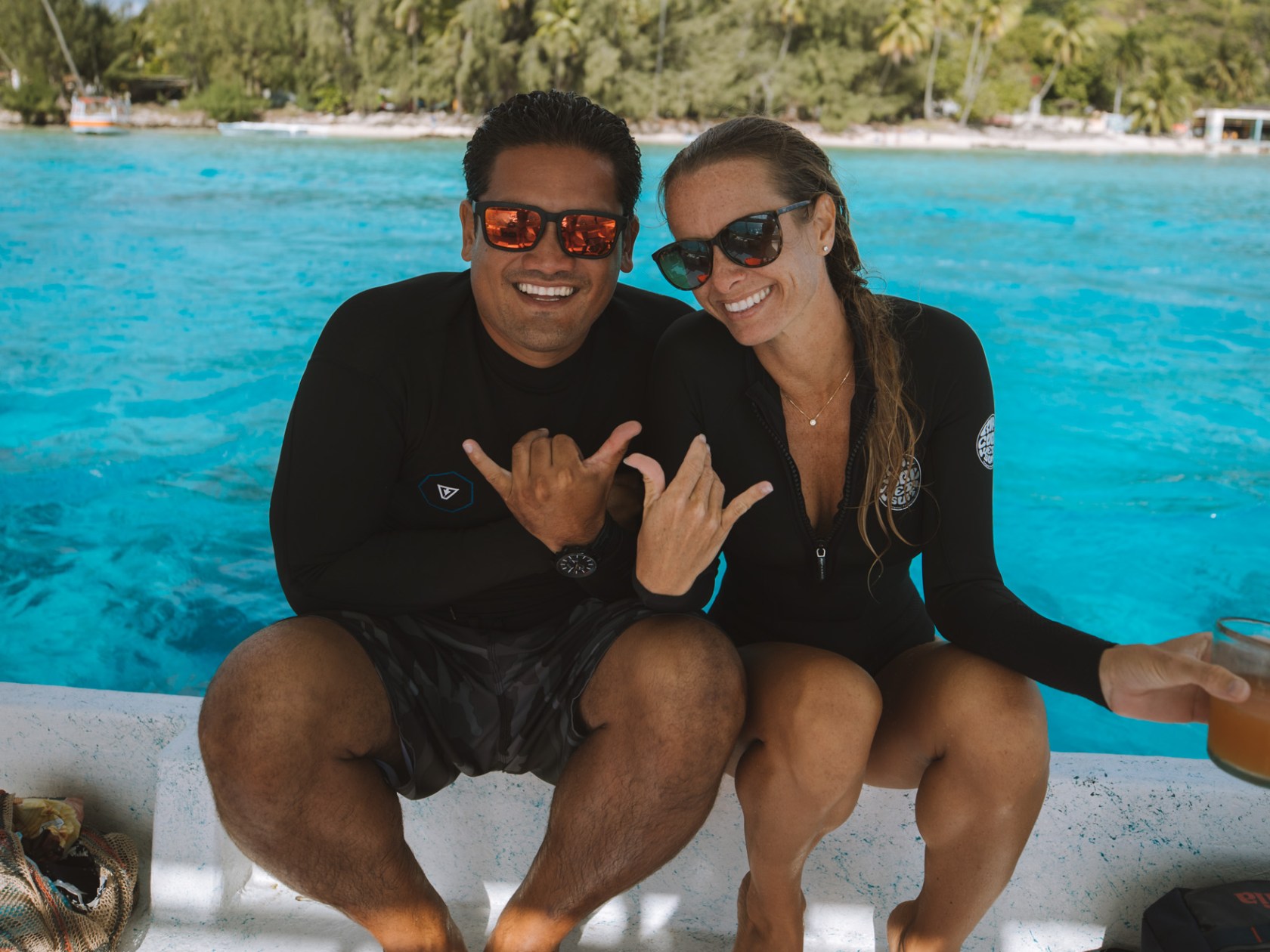 Two people in swimsuits on a boat, smiling with ocean background.