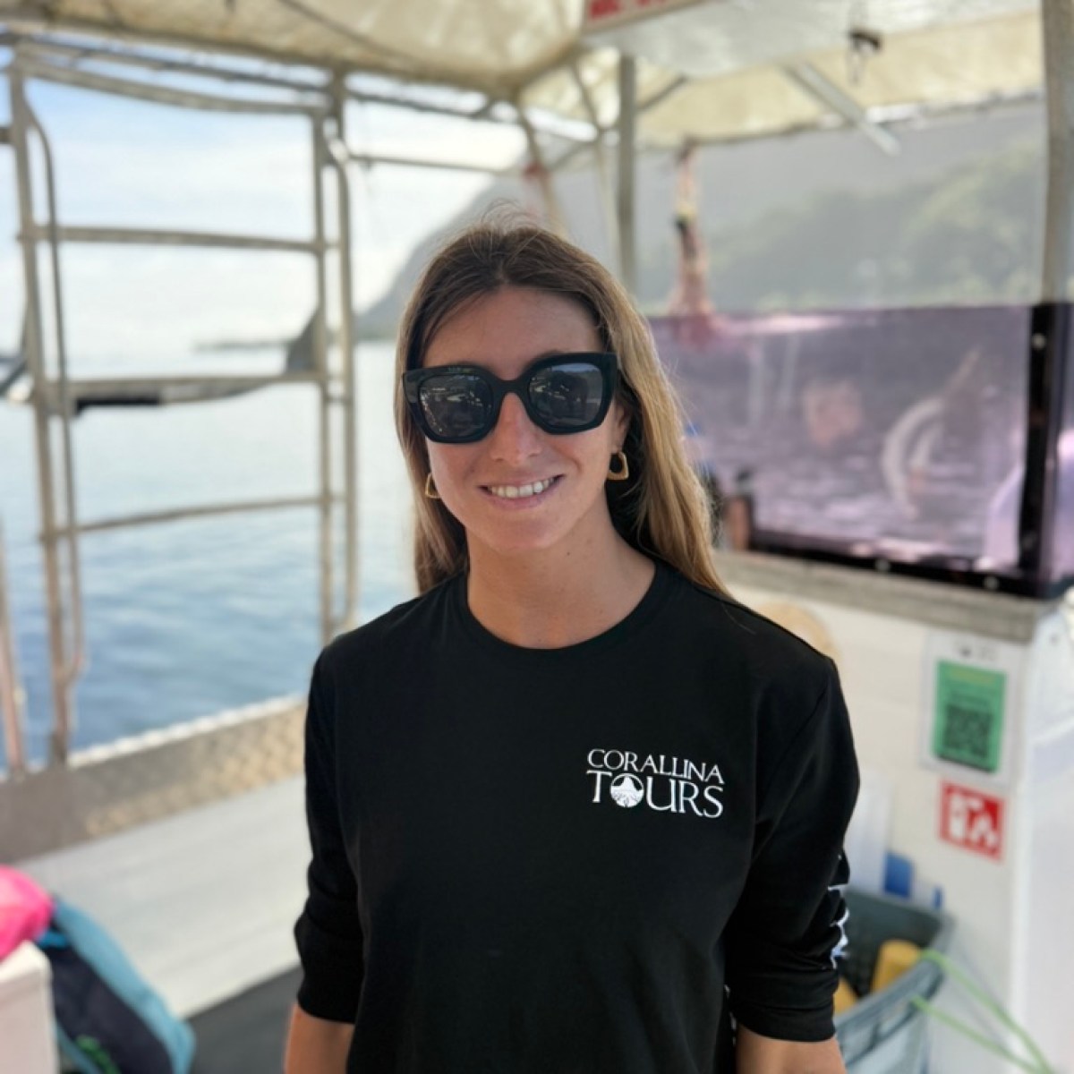 Person in sunglasses and black shirt on a boat with ocean in the background.