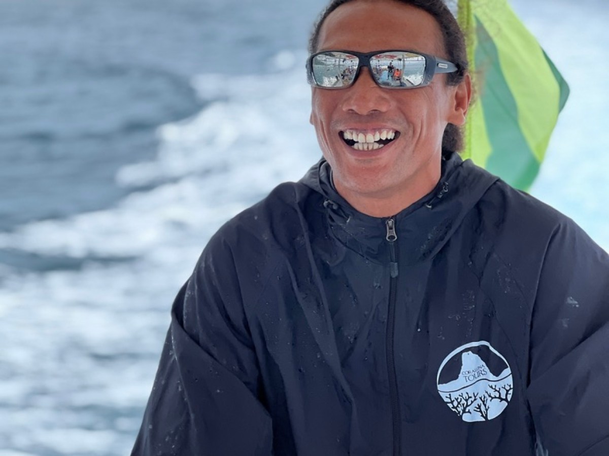 Person smiling while steering a boat, wearing sunglasses and a jacket.
